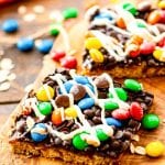 Bars topped with chocolate, m&m's, and white chocolate on wooden cutting board