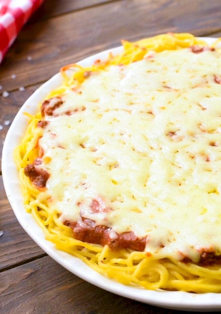 Baked Spaghetti Pie in white ceramic pie plate on wooden background with red checkered napkin in background.