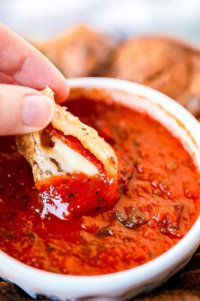 A cut open piece of pizza monkey bread being dipped in marinara sauce