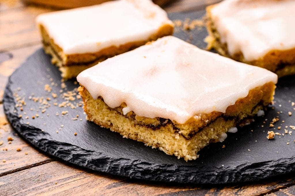 Cut Snickerdoodle Bars with frosting on a black slate piece