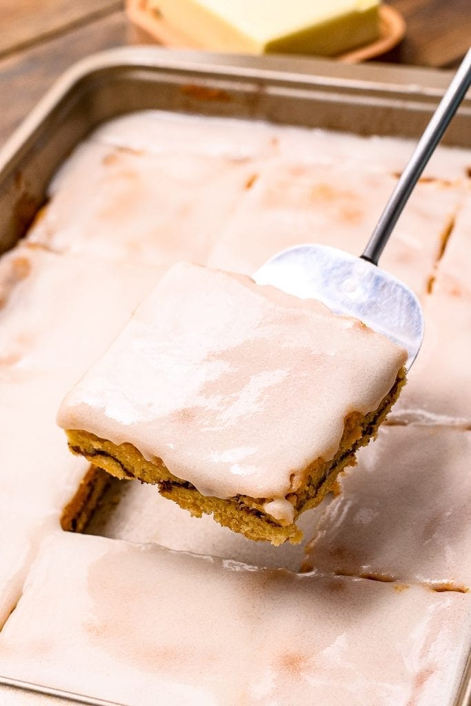 Metal spatula holding Snickerdoodle Bar above the pan of bars with frosting