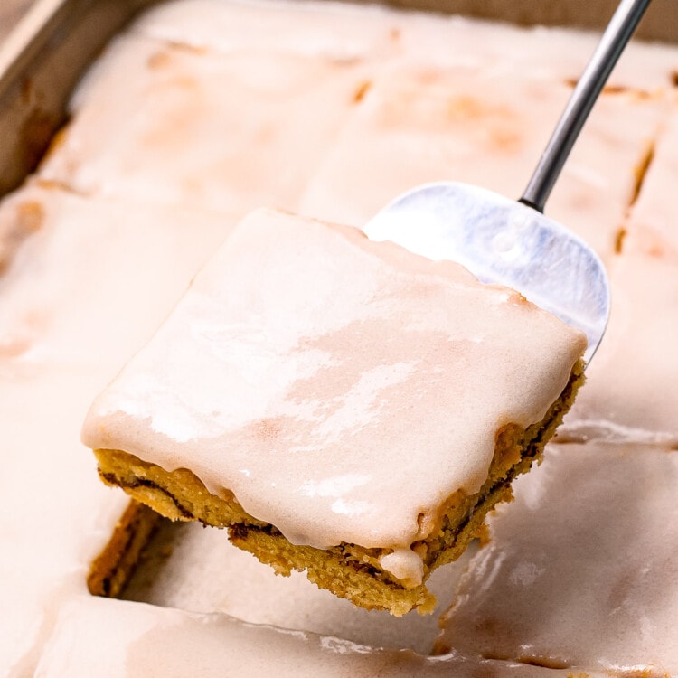 Metal spatula holding Snickerdoodle Bar above the pan of bars with frosting