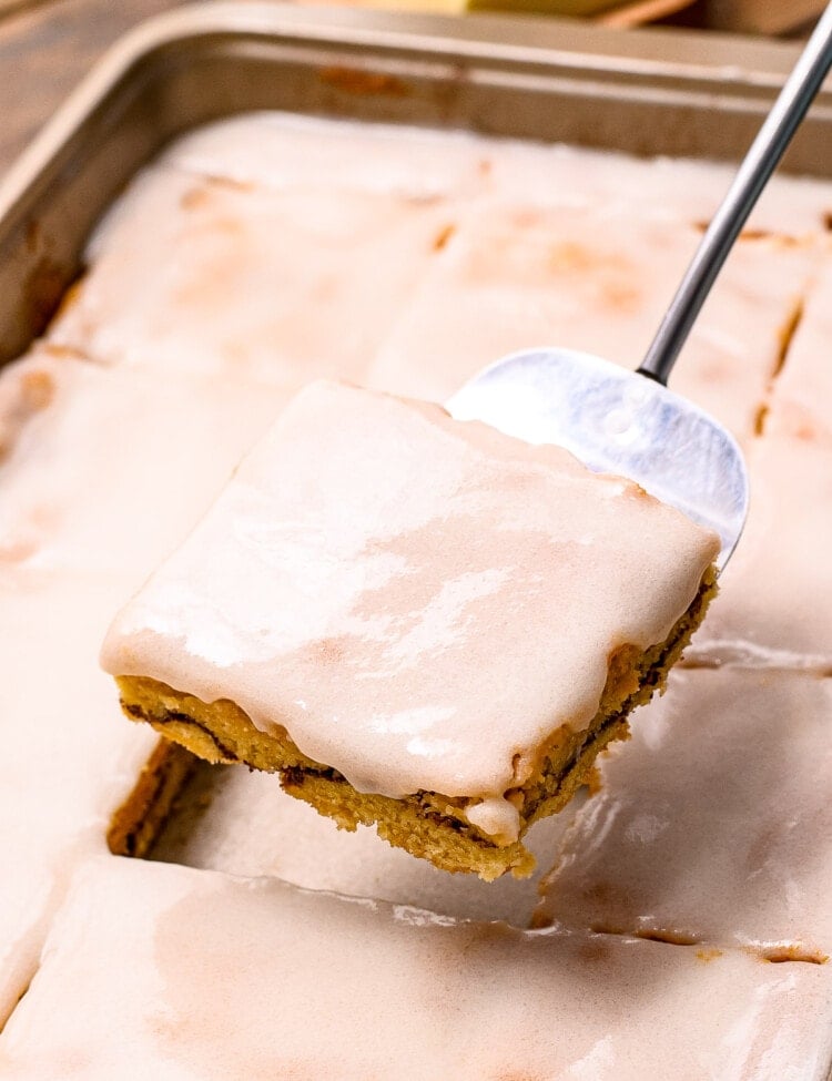 Metal spatula holding Snickerdoodle Bar above the pan of bars with frosting