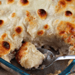 Chicken alfredo bubble up in a glass casserole dish with a serving missing and a spoon scooping some out