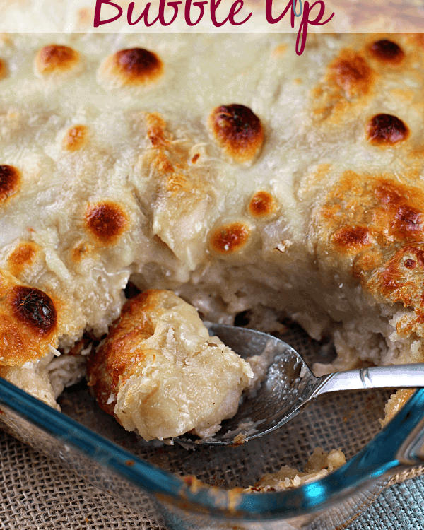 Chicken alfredo bubble up in a glass casserole dish with a serving missing and a spoon scooping some out