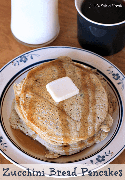 A short stack of zucchini bread pancakes topped with a pad of butter and syrup on a white plate in front of a glass of milk and a mug of coffee