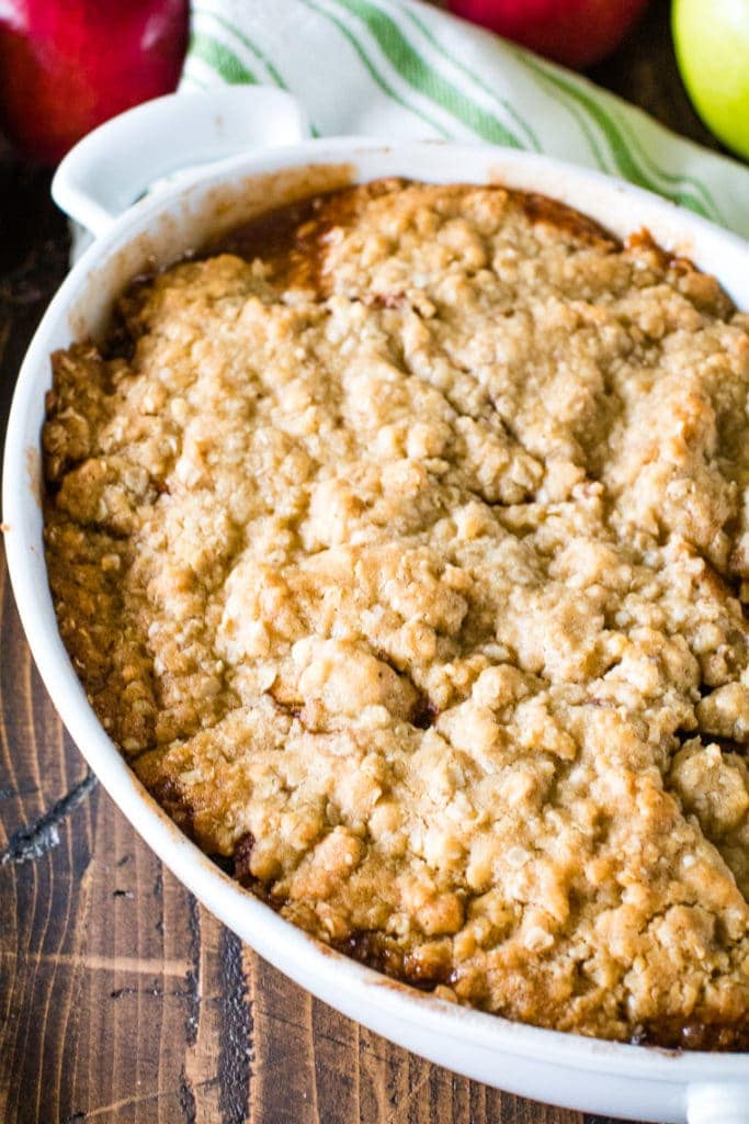 Apple Crisp in White Casserole Dish with a green striped napkin and apples in background