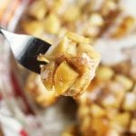 A bite of upside down caramel apple rolls on a fork being held over a glass pie plate containing the rest of the rolls