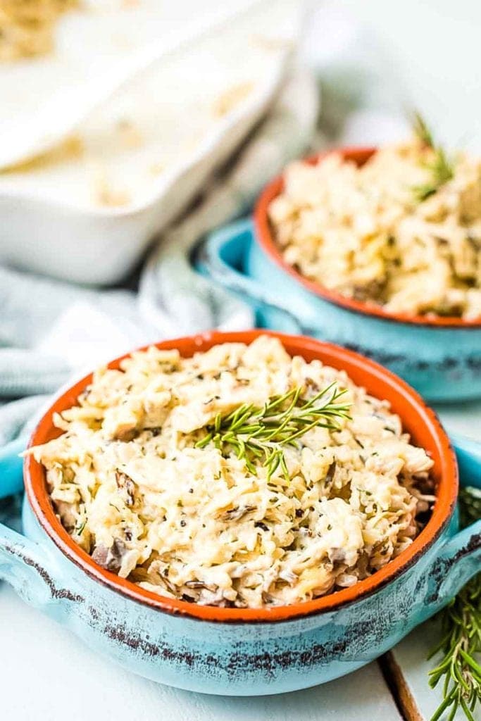 Blue Crock dishes with prepared Chicken and Wild Rice Casserole in them topped with rosemary for garnish