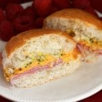 Ham, cheese, and poppy seed sandwich cut in half on a white plate with raspberries