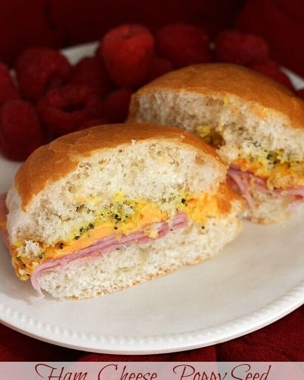 Ham, cheese, and poppy seed sandwich cut in half on a white plate with raspberries