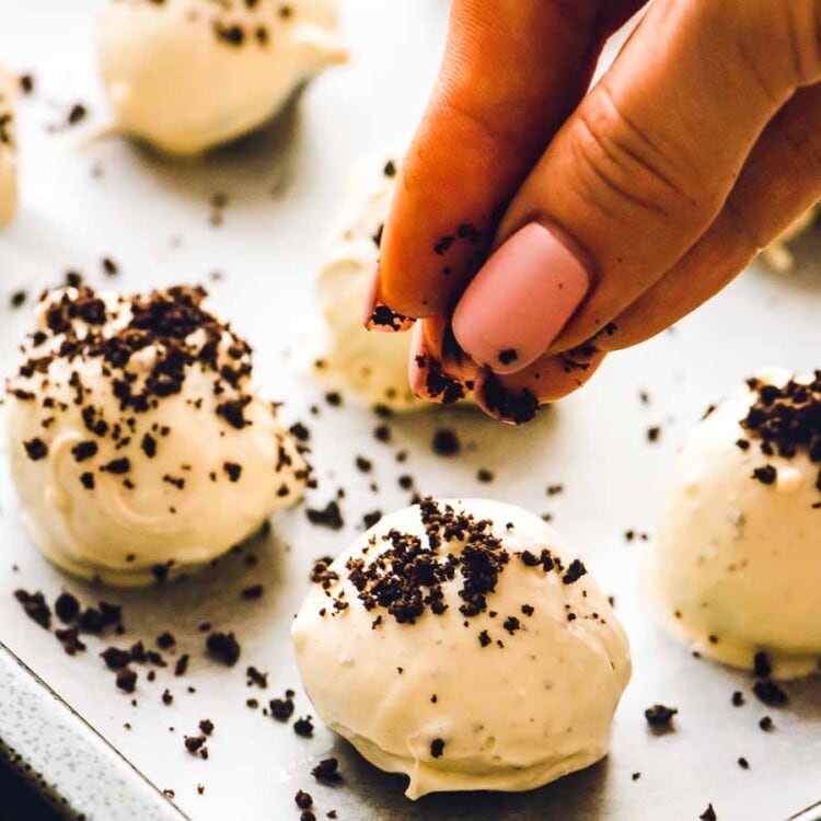 Sprinkling crushed up oreos over Oreo Balls on a baking sheet