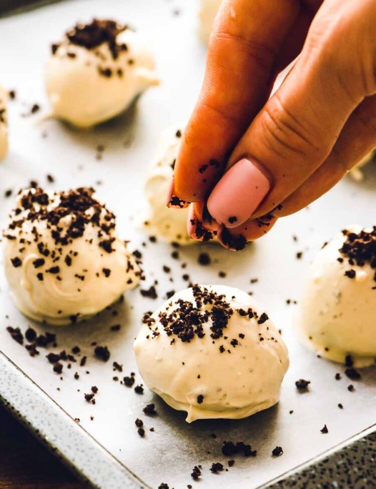 Sprinkling crushed up oreos over Oreo Balls on a baking sheet