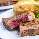 Sliced steak on white plate with baked potato sliced open in background
