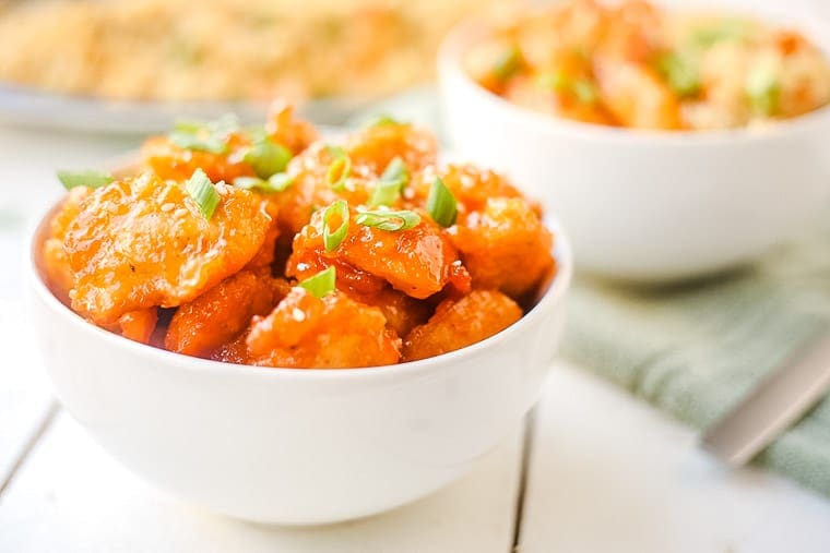 Two white bowls full of homemade baked sweet and sour chicken with sesame seeds and green onion for garnish