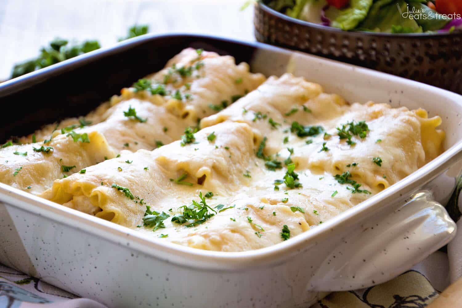 Lasagna roll ups topped with alfredo sauce and mozzarella cheese in square baking dish