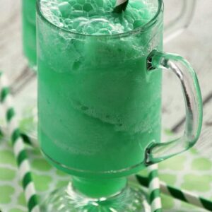 Two tall glass mugs of leprechaun floats with green and white striped straws