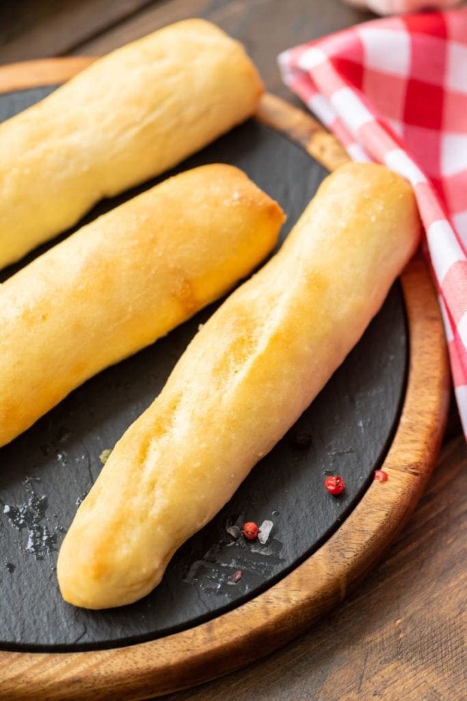 Platter with three breadsticks on it and red checkered napkin in background