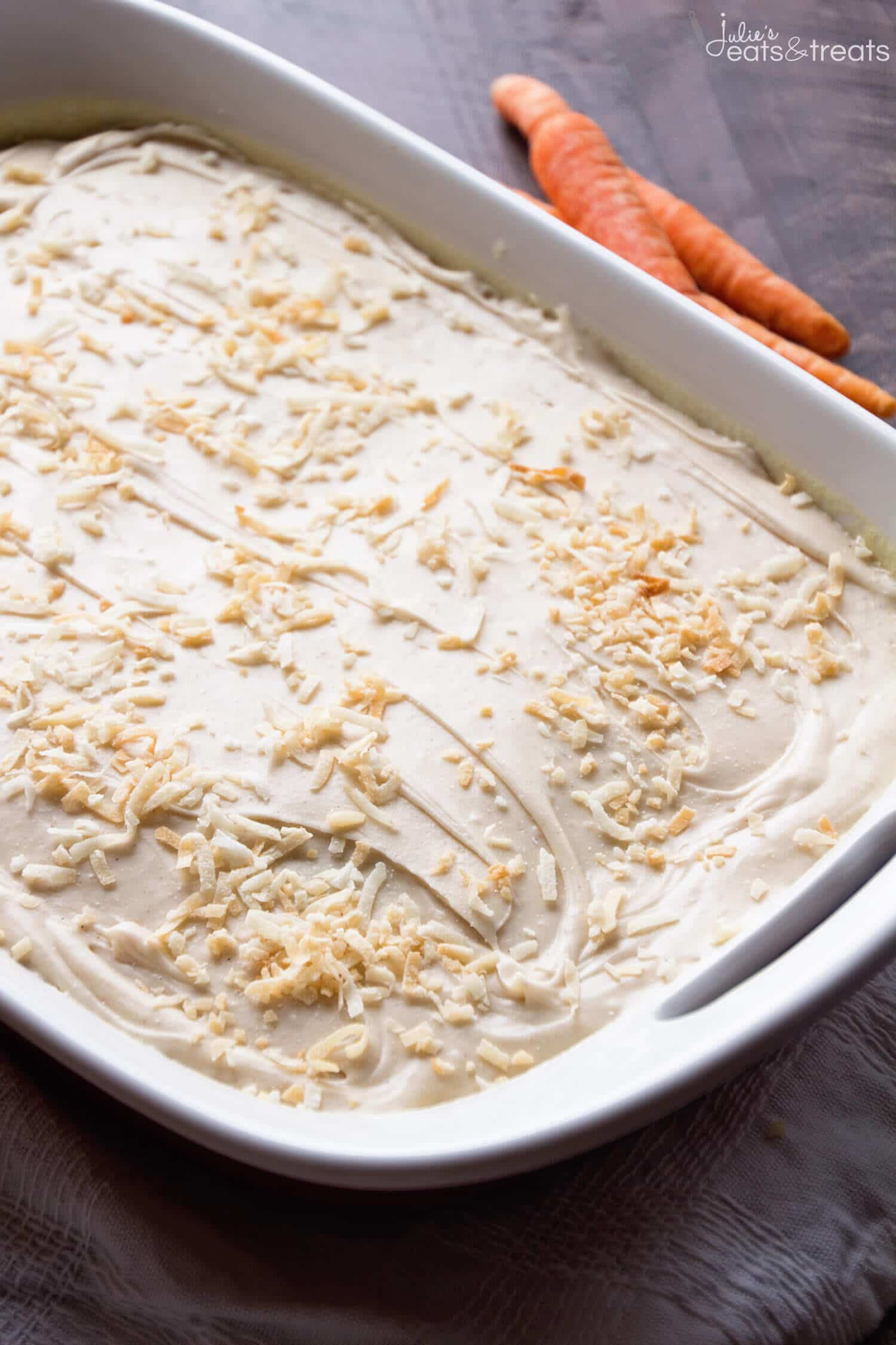 A pan with carrot poke cake in it and carrots lying next to it