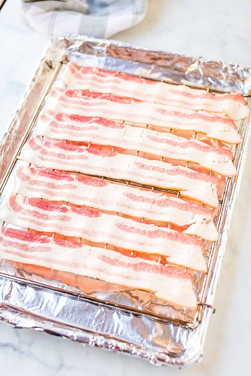 Strips of uncooked bacon on a wire rack over aluminum foil