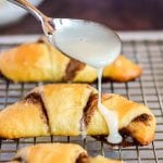 Spoon drizzling glaze across the top of a baked crescent roll