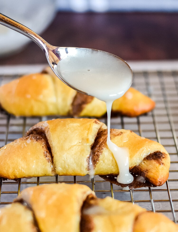 Spoon drizzling glaze across the top of a baked crescent roll