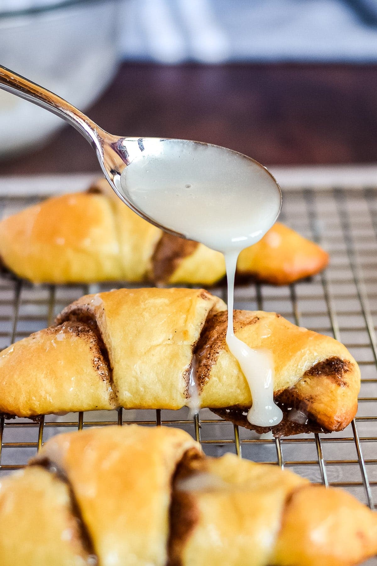 Spoon drizzling glaze across the top of a baked crescent roll