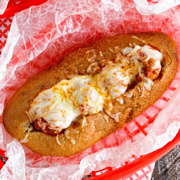 An overhead image of a meatball sub in a red plastic basket lined with wax paper