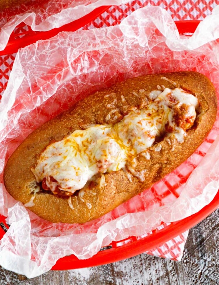 An overhead image of a meatball sub in a red plastic basket lined with wax paper