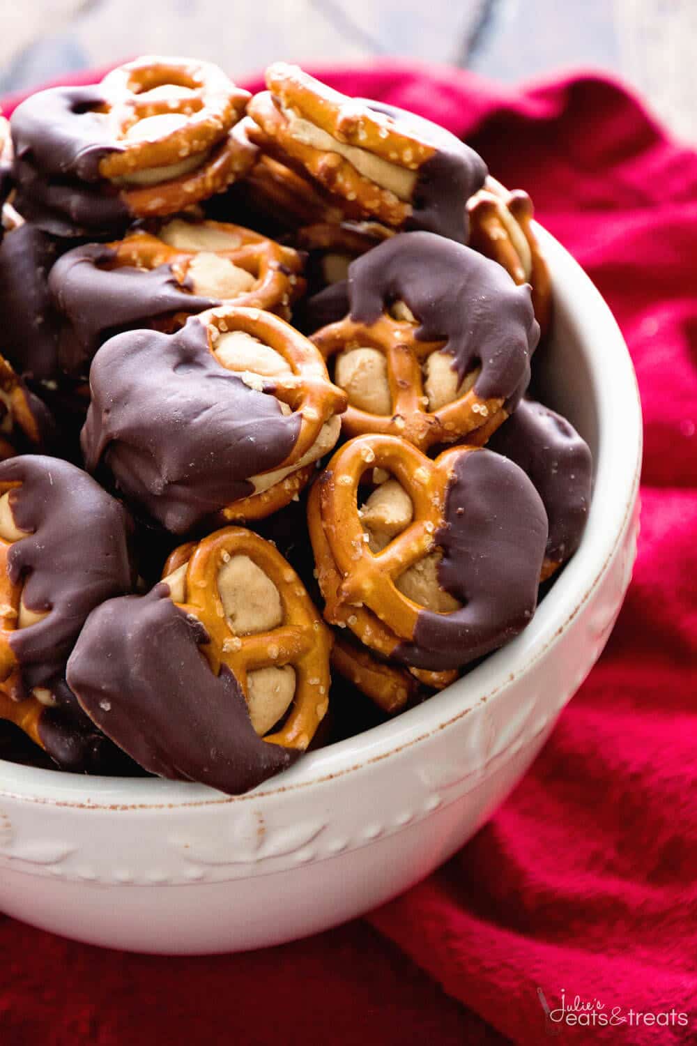 A white bowl full of chocolate covered peanut butter pretzels on a red napkin