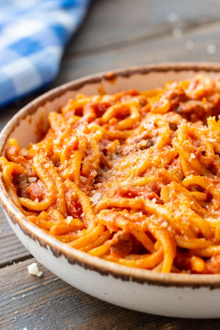 Wooden background with a bowl of spaghetti in it and blue and white checkered napkin ground in background