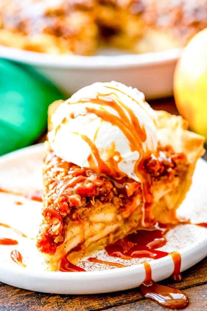 A white plate with a slice of Apple Crumb Pie topped with ice cream and caramel.