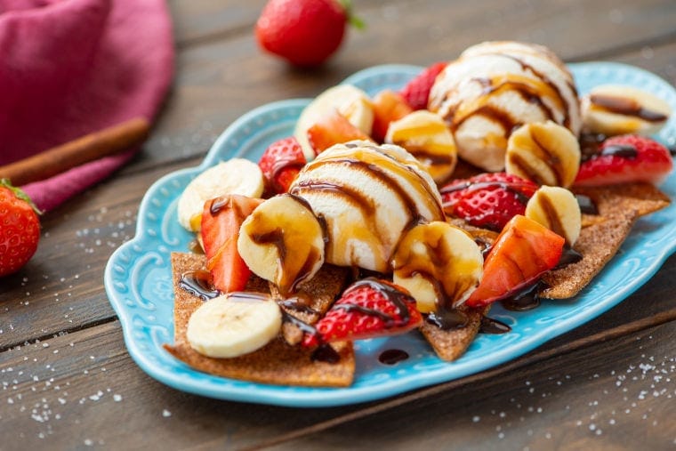 Wood background with blue platter with dessert nachos strawberries and red napkin in background