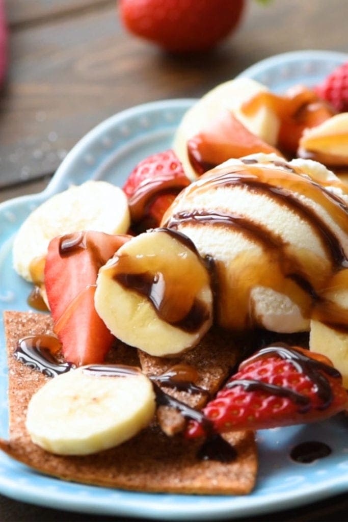 Blue platter with assembled dessert nachos; cinnamon tortilla chips, sliced strawberries, bananas, ice cream, syrups