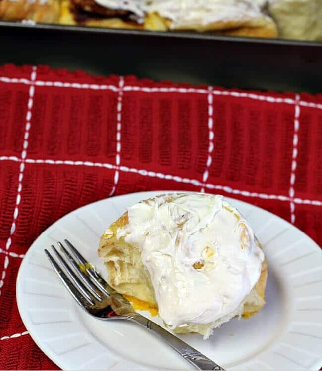 A three ingredient cinnamon roll on a white plate with a fork sitting on a red kitchen towel