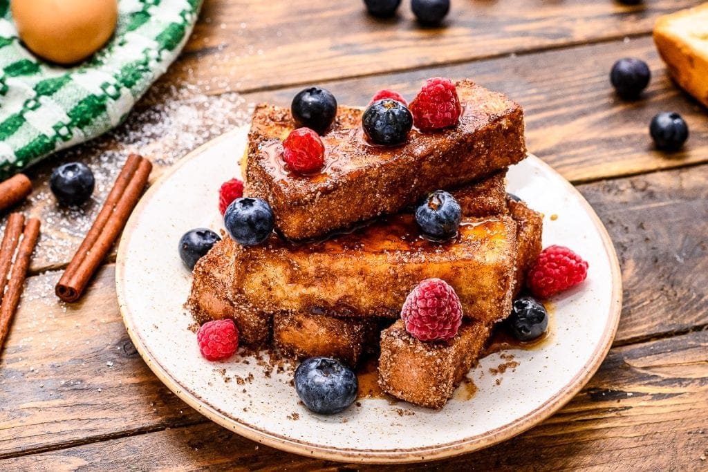 stack of french toast sticks with syrup and berries topping it on a plate