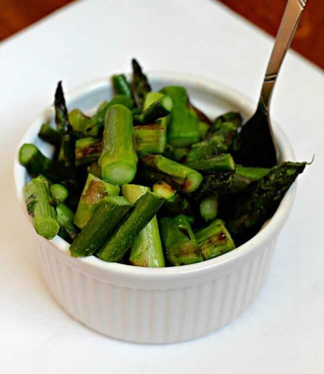A white bowl of skillet asparagus with a fork in it sitting on a white plate