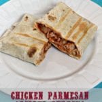 Chicken parmesan grilled burrito cut in half on a white plate sitting on a blue cloth napkin