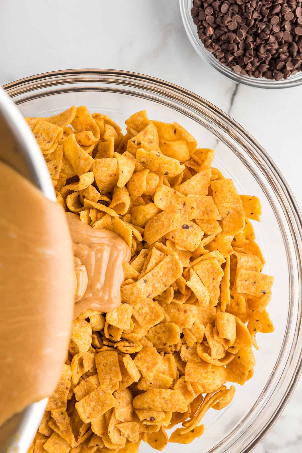 Pouring peanut butter sauce over Fritos in bowl