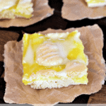 Three lemon pie bars on pieces of parchment paper