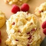 White chocolate raspberry cookies stacked on a baking sheet with raspberries