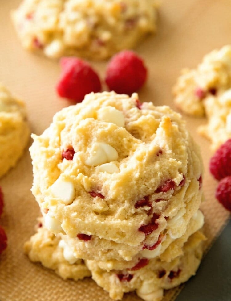 White chocolate raspberry cookies stacked on a baking sheet with raspberries