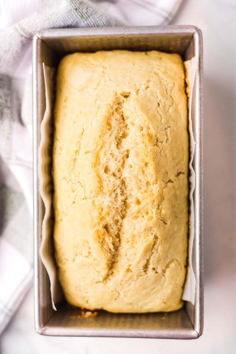 Overhead image of a baked loaf of beer bread in pan that is lined with parchment paper.