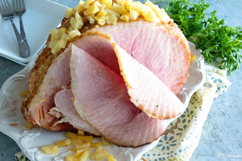 Spiral Ham sliced with pineapple piled on top and on white serving platter with napkin under it
