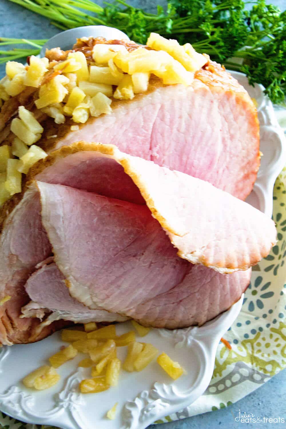 White serving plate with spiral ham and pineapple on it sliced