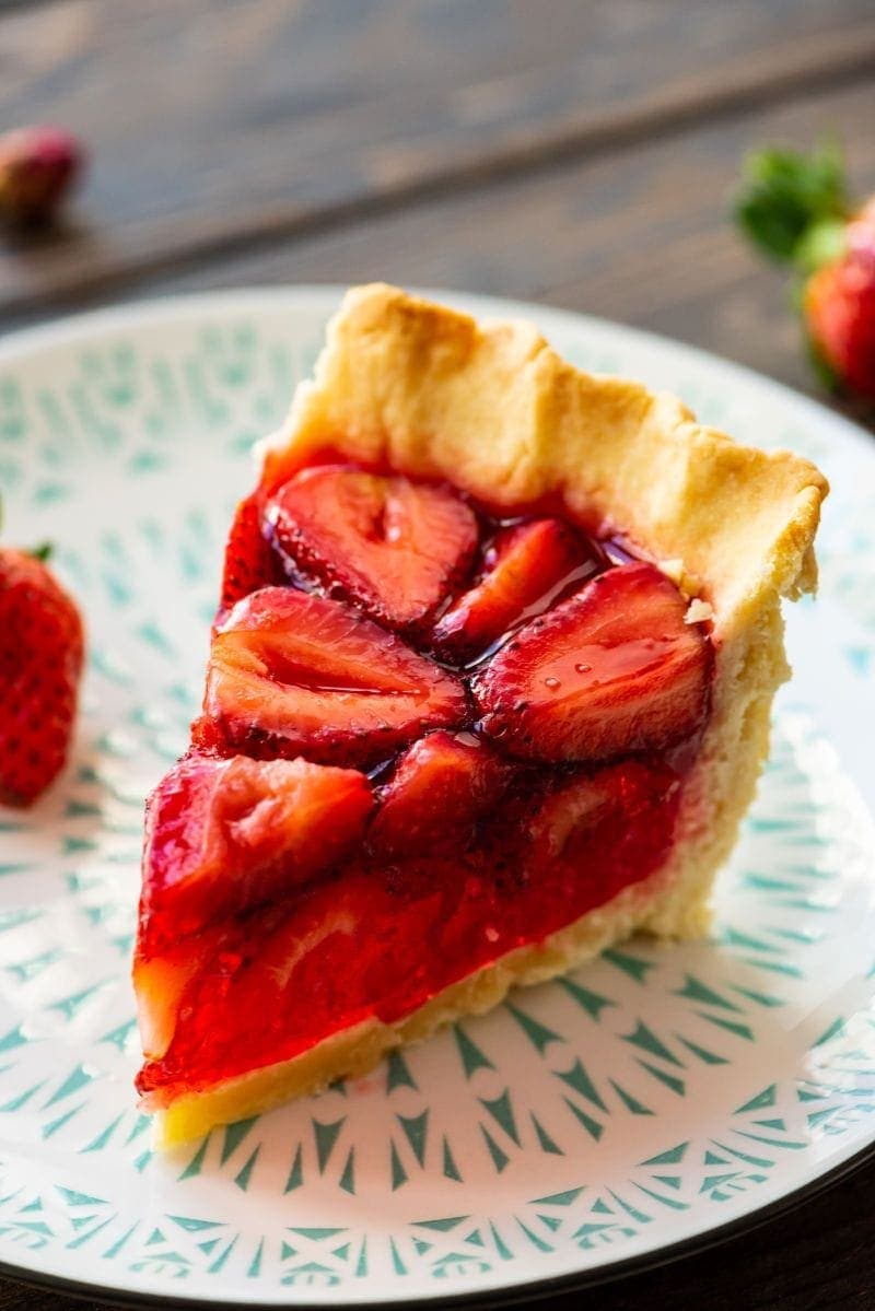 Slice of pie on white and green plate and fresh strawberry in background