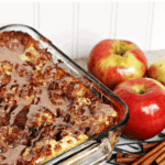 Square glass casserole dish of apple cinnamon cream cheese pull apart on a table with apples and cinnamon sticks