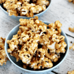 Two blue bowls of peanut butter cashew popcorn spilling out onto a table