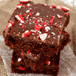 Three peppermint buttermilk brownies stacked on a piece of wax paper sitting on a burlap place mat