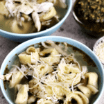 Two blue bowls of pesto chicken tortellini soup topped with parmesan cheese